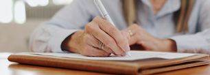 A woman focused on writing on a piece of paper with a pen, sitting at a desk.