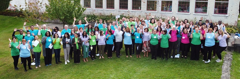 A group of people wearing green, blue and pink shirts standing outside, cheering with excitement.