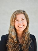 person with long hair wearing a black blazer smiling at camera