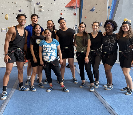 Group of students standing together smiling in front of a rock wall.