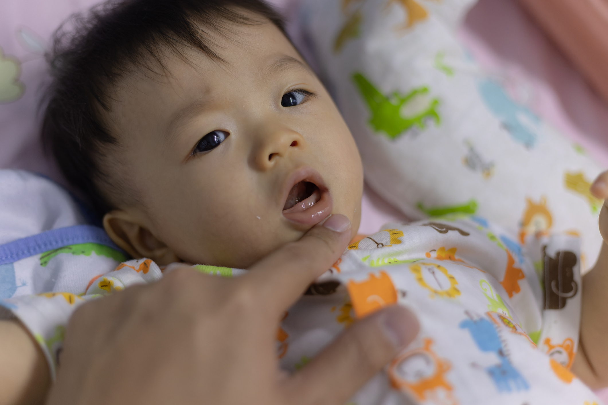 a parent gently opens a baby's mouth to see their gums.