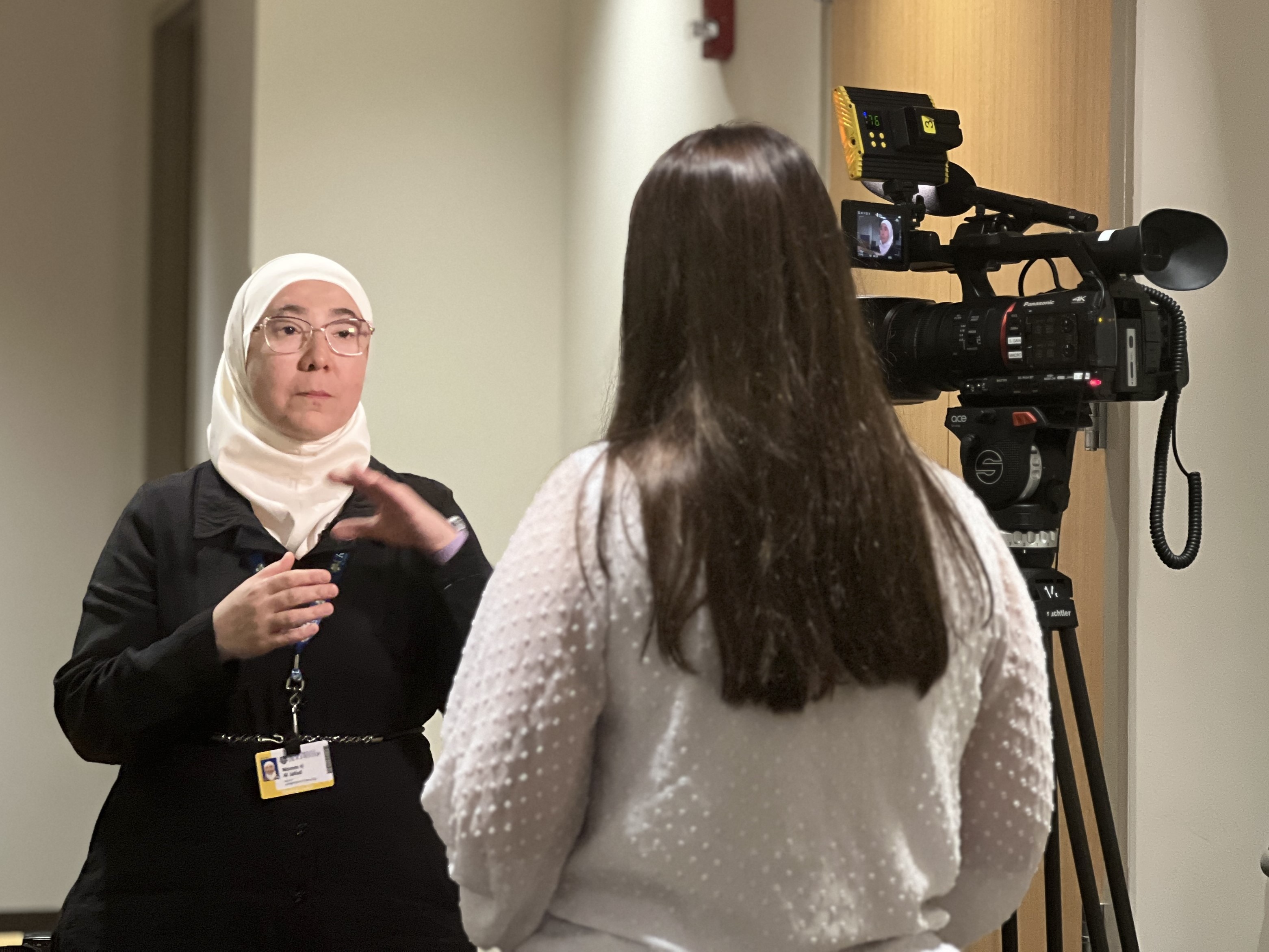 a woman speaks to a reporter while being recorded by a camera.