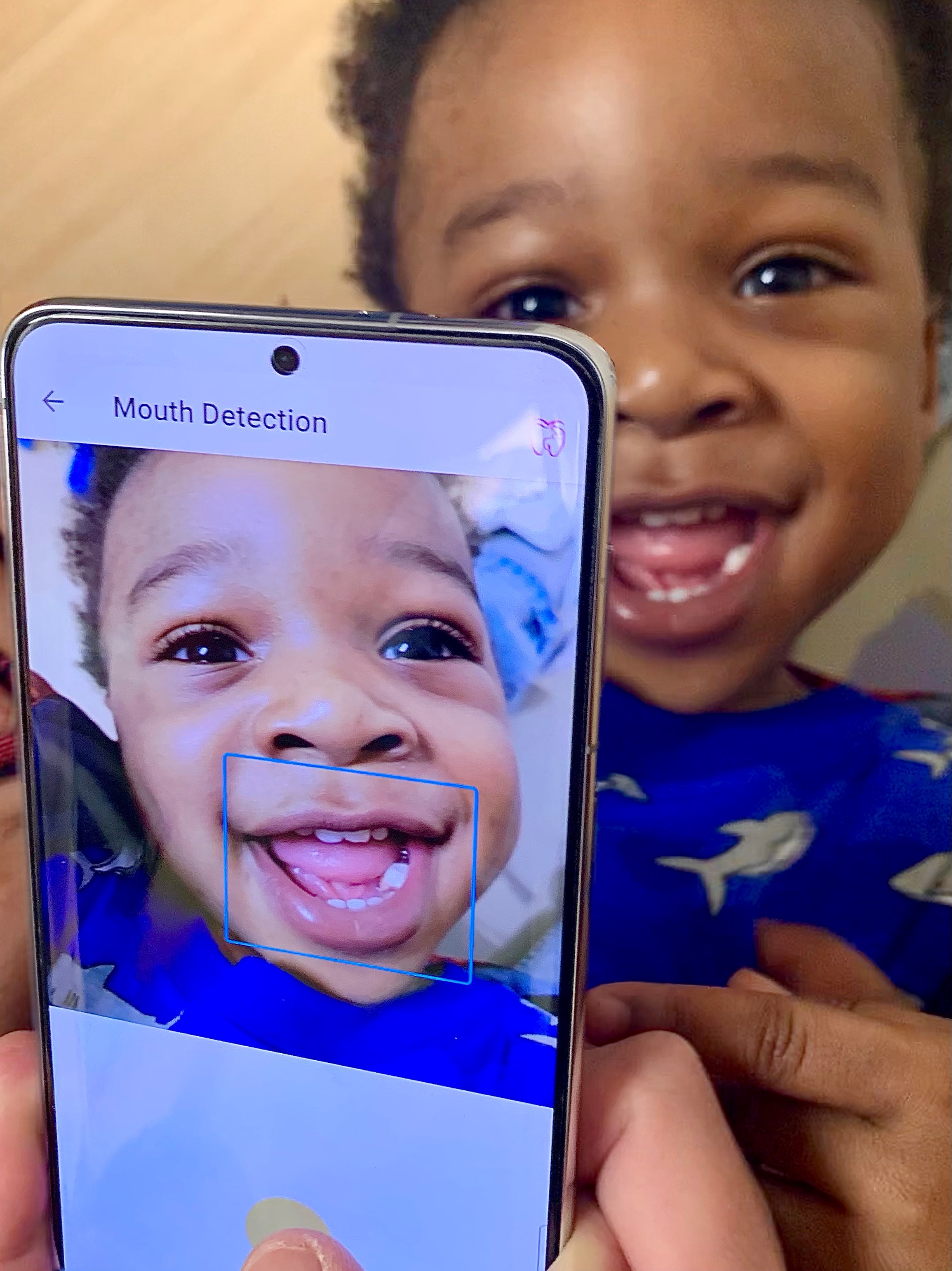 a phone camera captures a picture of a smiling baby's mouth.