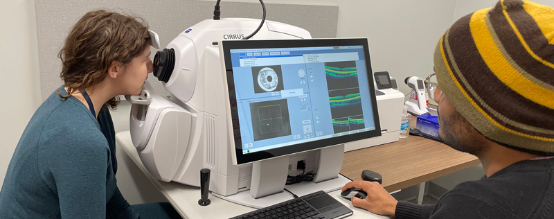 women looking into eye machine while male researcher views results on screen