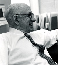 Casual photograph of Bibby in the office, he is seated and smiling.