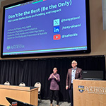 Tony Pisani presenting at front of auditorium with ASL interpreter