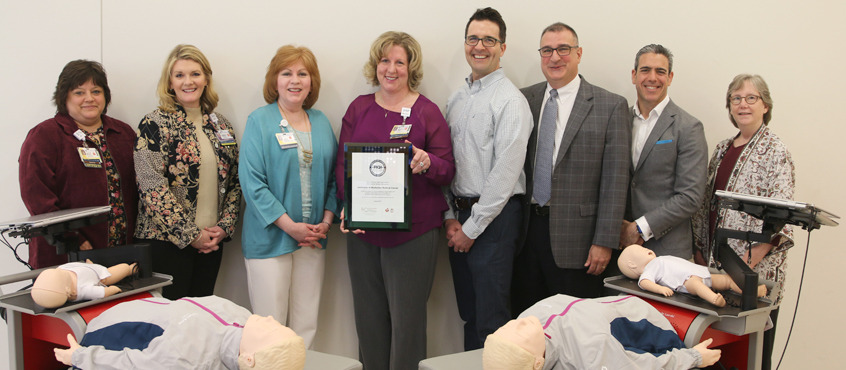 Nurse leaders, Friends of Strong, American Heart Association, and Laerdal Medical representatives pose with two of the mobile training units for an award presentation.