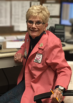 Rose turns her chair to smile for a picture while volunteering at the information desk in the Family Waiting Room.