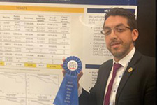 Victor Sandoval Holding a Ribbon Next to His Poster